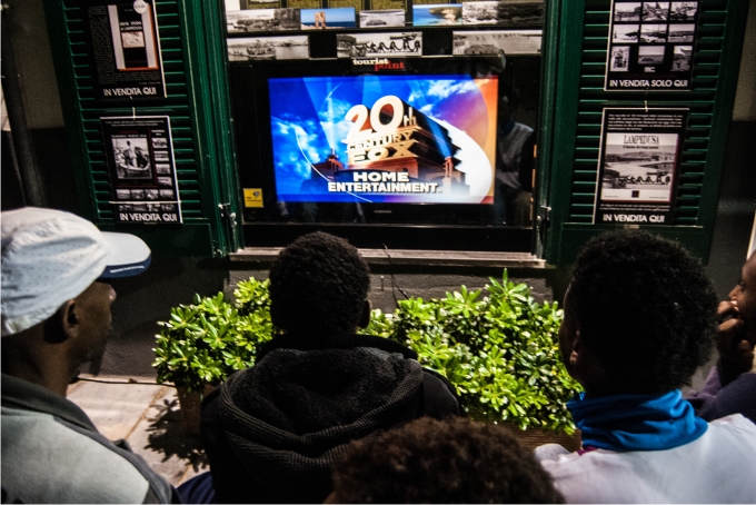 Chicos eritreos miran una película en inglés delante del Archivo Histórico de Lampedusa.