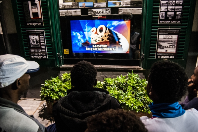 Lampedusa, entre el limbo y el edén 7 Chicos eritreos miran una película en inglés delante del Archivo Histórico de Lampedusa.