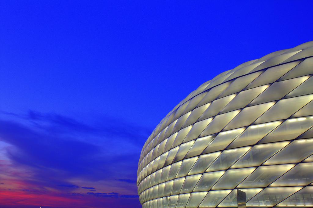 Rodeado de un cielo azul y rojo, el Allianz Arena de Munich se ilumina en blanco para un partido de la selección alemana de fútbol. Foto de Mohamed Yahya (CC)