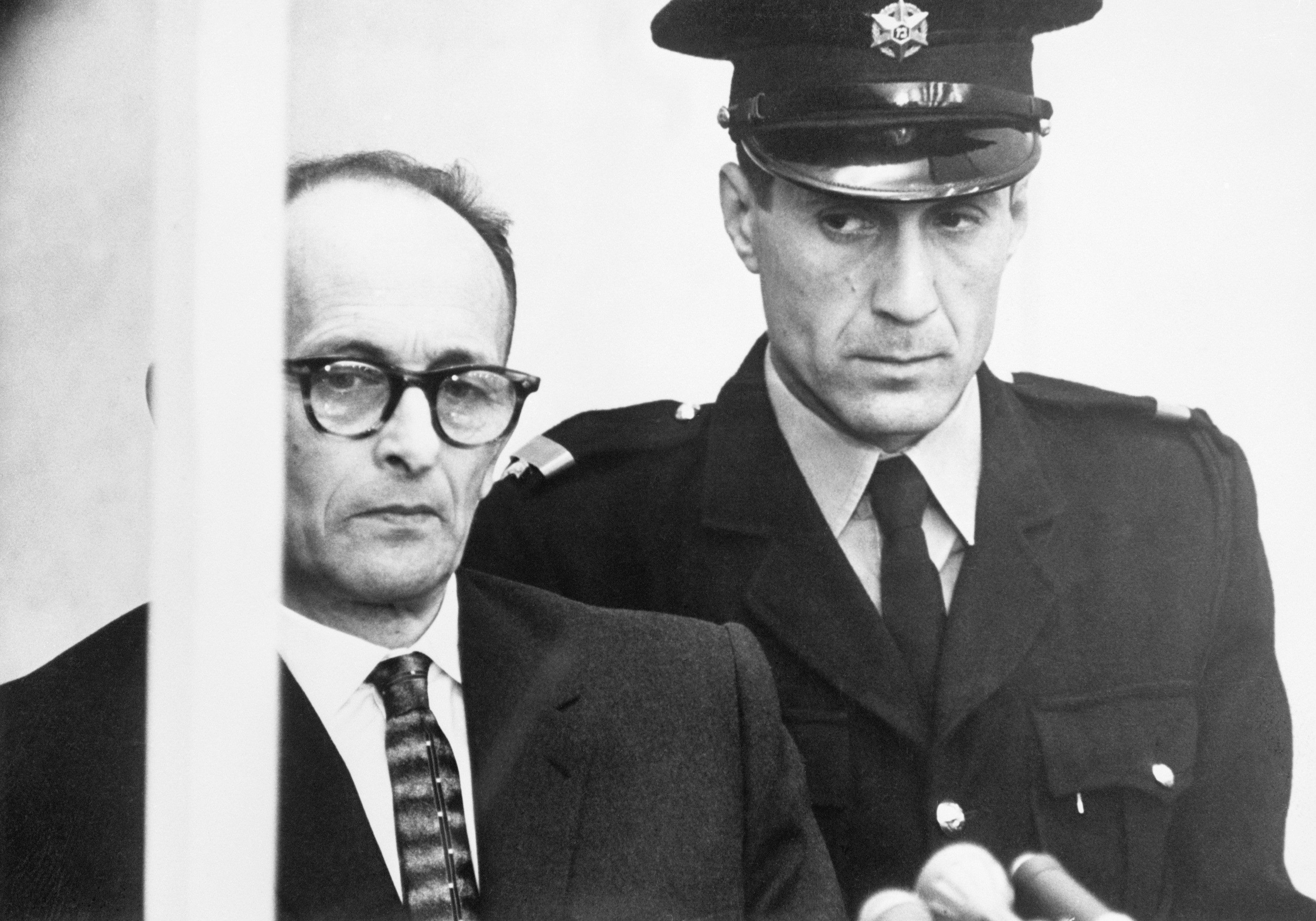 11 Apr 1961, Jerusalem, Israel --- Original caption: 4/11/1961-Jerusalem, Israel- A thin faced Adolf Eichmann listens to the reading of a 15 count indictment, accusing him of the murder of millions of Jews during World War II, as a guard stands beside him (R), April 11. The reading of the charges at the trial's opening took an hour and 15 minutes. --- Image by © Bettmann/CORBIS