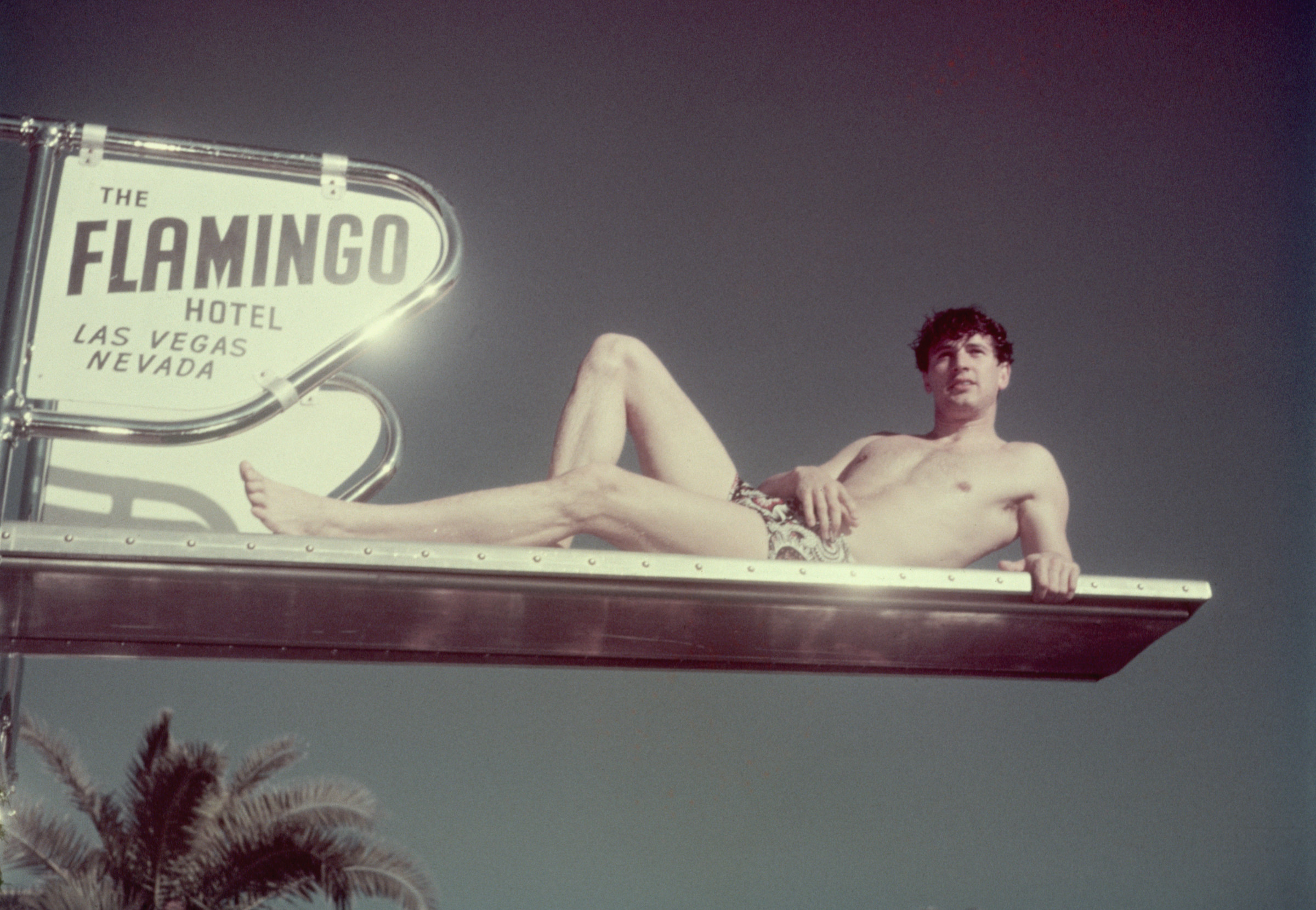 ca. 1940-1959, Las Vegas, Nevada, USA --- Original caption: Las Vegas: Photo shows Rock Hudson (1925-1985) lying sideways on the diving board of the pool at the Flamingo Hotel in Las Vegas. Ca. 1940s-1950s. --- Image by © CORBIS