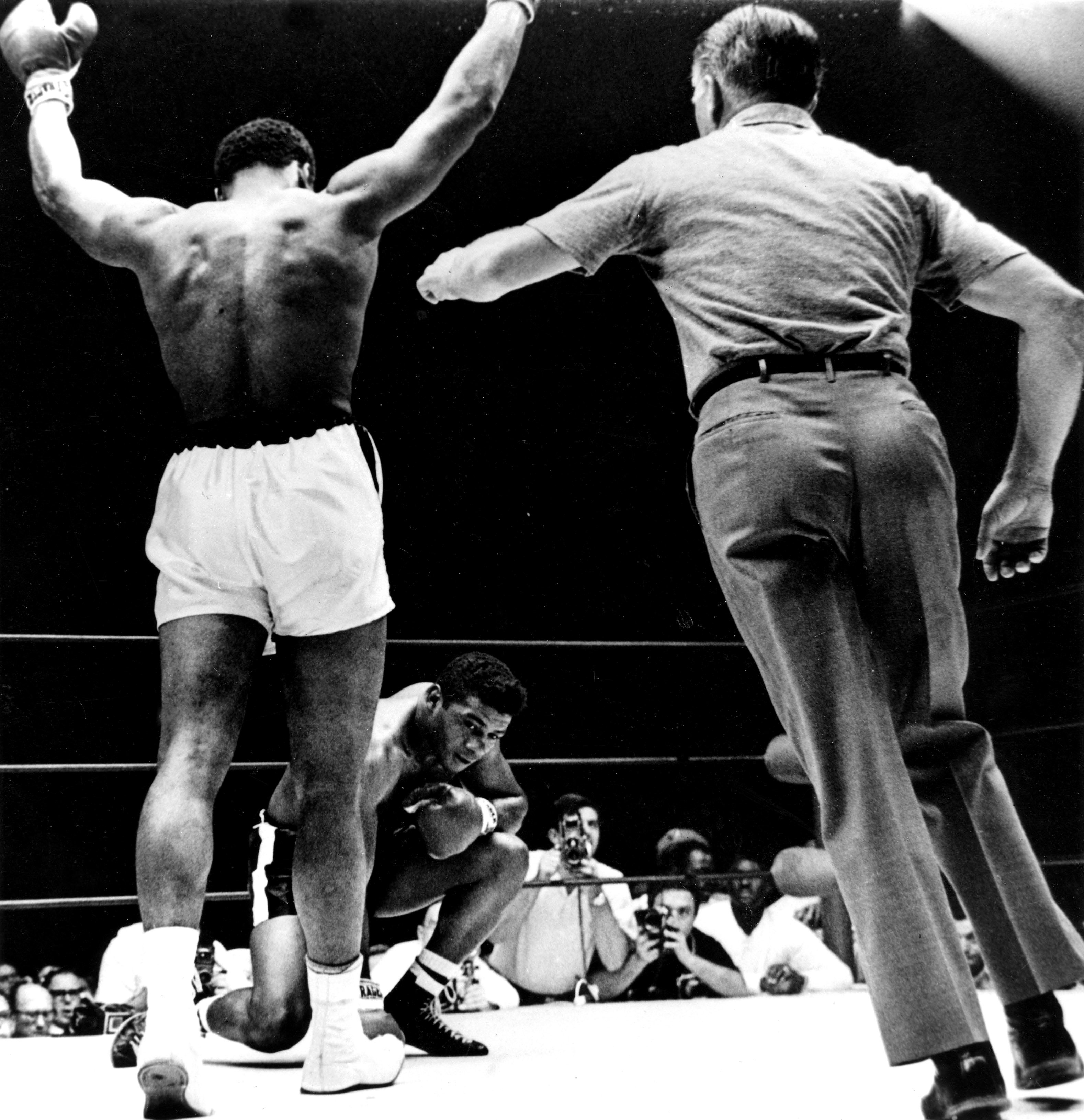Cassius Clay with arms raised, is waived to the neutral corner as Floyd Patterson (kneeling) takes a mandatory count of eight in the 6th round of their title fight in Las Vegas. Clay won on a technical knock-out in the 12th round to retain his title. The referee, Mr Krause, had to warn Clay for talking to Patterson early in the fight. "Clay tried from the first round to humiliate Patterson", Mr Krause said. "He tortured him with remarks like, 'Come on American, come on white American'". After the fight, Clay showered Patterson with unstinting praise and then typically demanded plenty of credit for himself from the "American Public". Clay spent nearly 15 minutes in the ring after the fight delivering a long impassioned oration, before finally heading for his dressing room. 22nd November 1965.