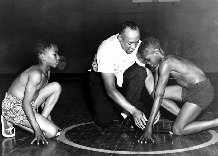 America's great Olympic track star Jesse Owens is showing two boys from the South Side Boys Club the starting position that brought him fame. Rajah Latimore (left) Sherman Davis 1st July 1954