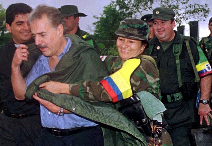 A rebel woman of the Revolutionary Armed Forces of Colombia (FARC), covers Colombian President Andres Pastrana from the rain before the start of a meeting in Los Pozos in Colombia's southern demilitarized zone, February 8, 2001. Pastrana met rebel leader Marulanda in an attempt to revive a stuttering two-year old peace drive. REUTERS/Guillermo Tapia-Ancol