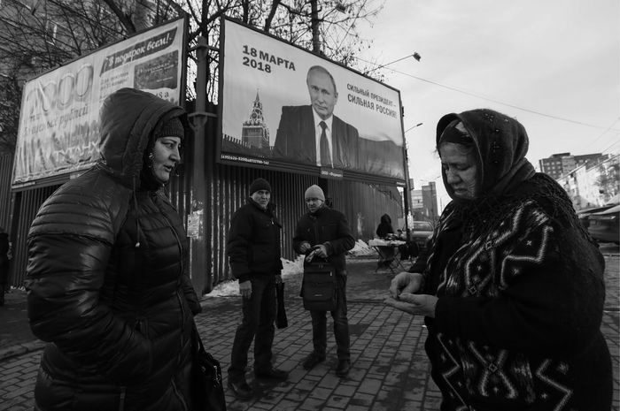 Women talk near a board, which advertises the campaign of Russian President Vladimir Putin ahead of the upcoming presidential election, in a street in Tula