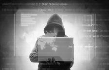 Hacker in black hoodie holding laptop with virtual display server data, chart bar, binary code and world map over dark background