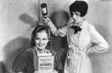 La escritora y guionista Anita Loos (derecha) bromea en el set de 'Red-Headed Woman' con la actriz Jean Harlow, que sostiene el libro Los caballeros las prefieren rubias'. Imagen MGM.